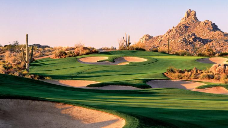 Golf green and sculpted bunkers ringed by saguaros below a granite boulder peak