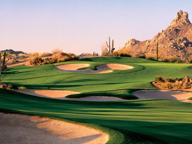Golf green and sculpted bunkers ringed by saguaros below a granite boulder peak