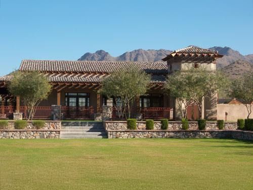Low tile-roofed clubhouse with a stone base and deep shaded porch across a wide lawn, mountains rising behind