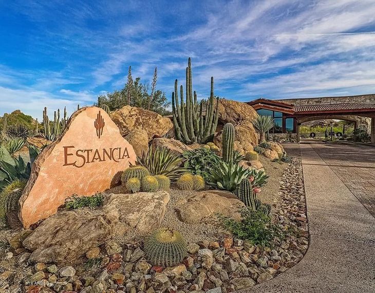 Carved Estancia entry monument boulder amid barrel cacti beside the stone gatehouse