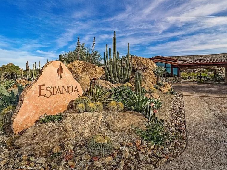 Carved Estancia entry monument boulder amid barrel cacti beside the stone gatehouse