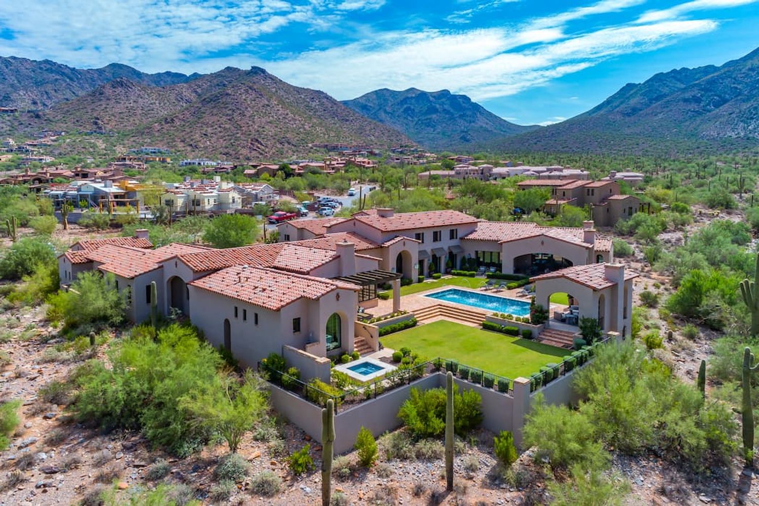 Aerial red-tile-roofed Spanish Colonial estate with pool and lawn below rugged mountains