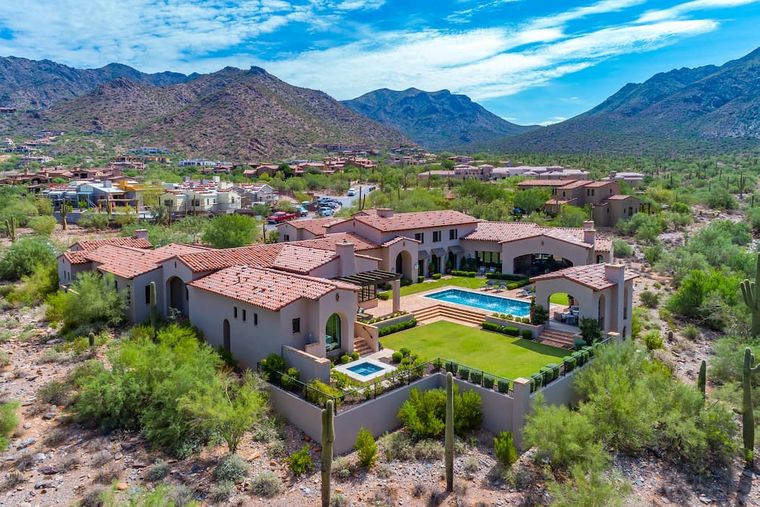 Aerial red-tile-roofed Spanish Colonial estate with pool and lawn below rugged mountains