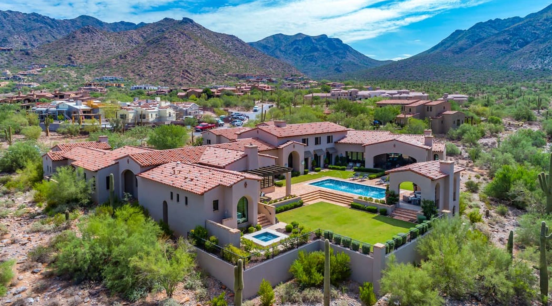 Aerial red-tile-roofed Spanish Colonial estate with pool and lawn below rugged mountains