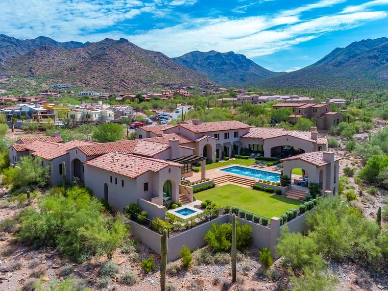 Aerial red-tile-roofed Spanish Colonial estate with pool and lawn below rugged mountains