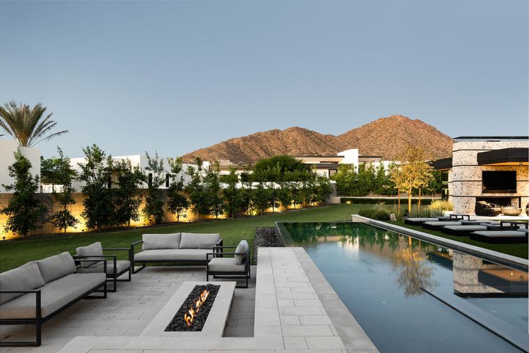 Contemporary home with lap pool and linear fire feature below a desert mountain at dusk