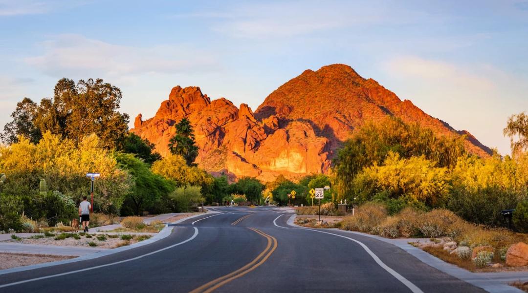 Two-lane road curving toward a red rock mountain glowing at golden hour