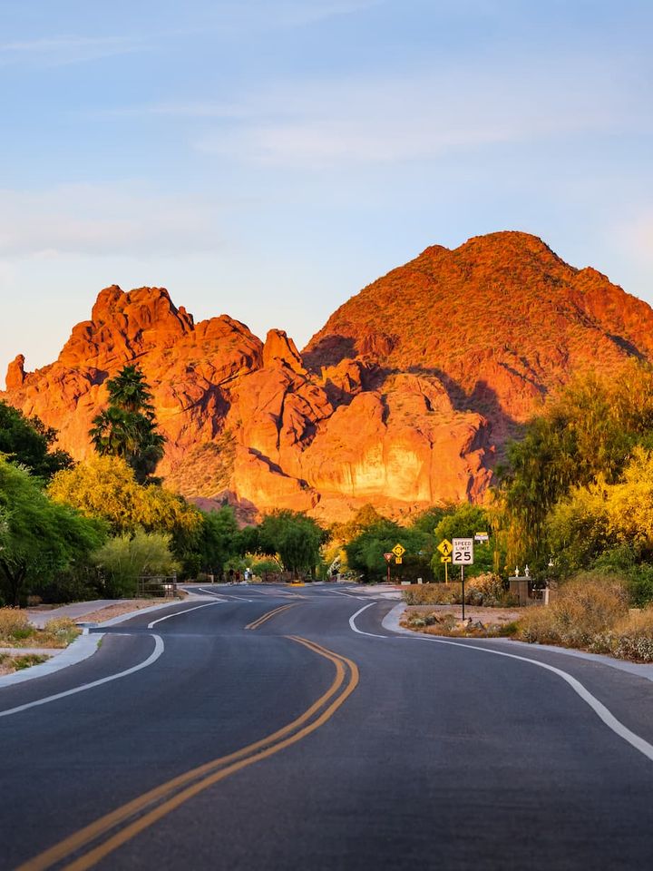 Two-lane road curving toward a red rock mountain glowing at golden hour
