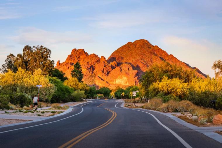 Two-lane road curving toward a red rock mountain glowing at golden hour