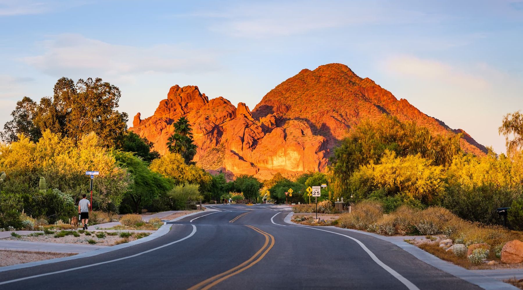 Two-lane road curving toward a red rock mountain glowing at golden hour