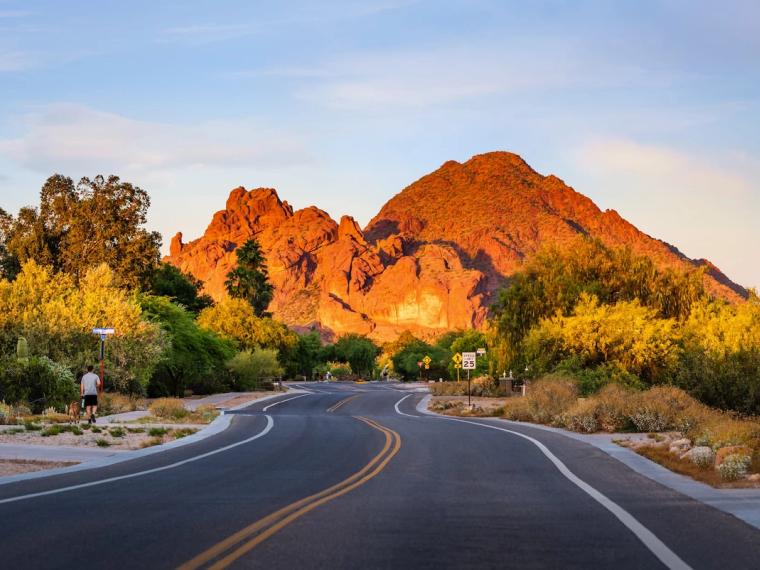 Two-lane road curving toward a red rock mountain glowing at golden hour