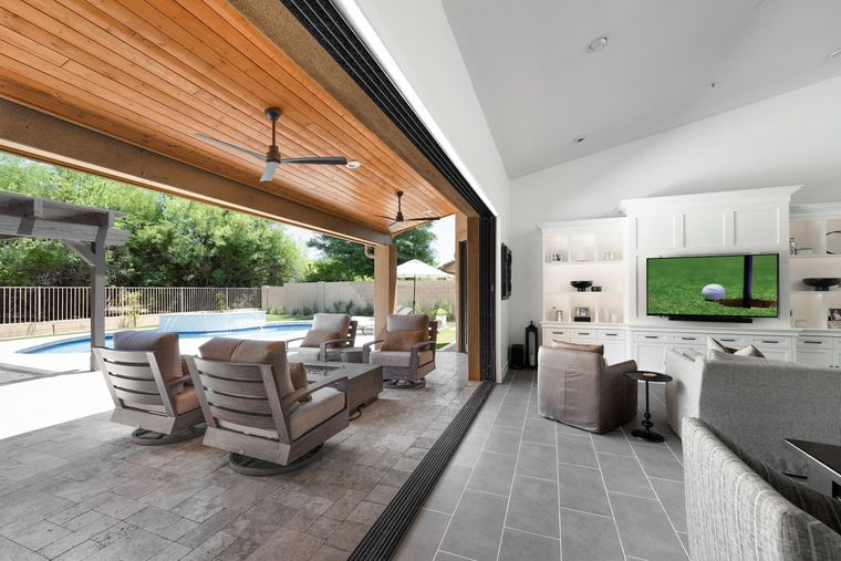 Living room opening through a full glass wall to a covered patio and pool