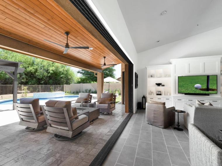 Living room opening through a full glass wall to a covered patio and pool