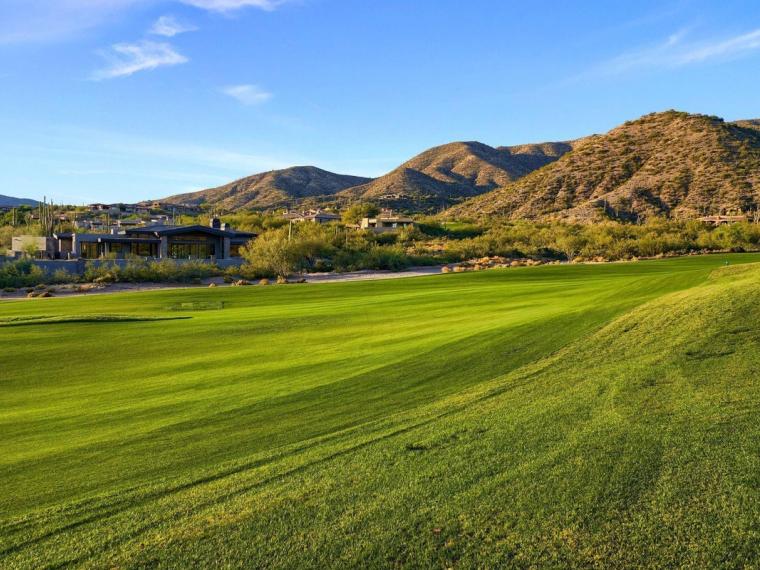 Broad sunlit fairway sweeping toward a scrub-covered mountain, low homes tucked along its base