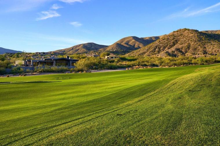 Broad sunlit fairway sweeping toward a scrub-covered mountain, low homes tucked along its base