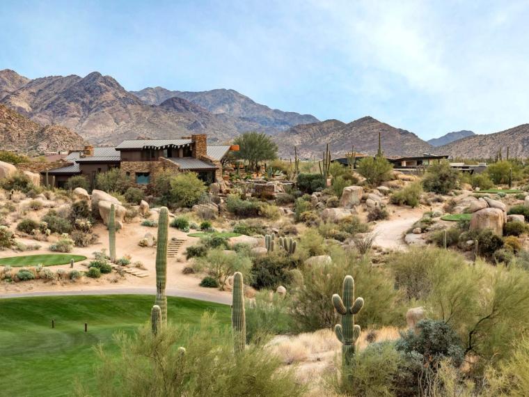 Low stone clubhouse set among saguaro and boulders above a green fairway, a long mountain ridge rising behind it