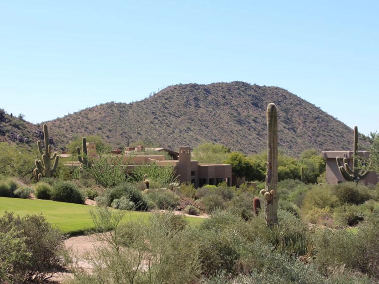 Desert homes below a peak, with golf turf and saguaro in front