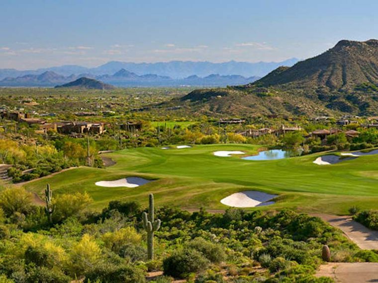 Manicured golf fairway with sand bunkers and a pond ringed by saguaro-studded desert hills