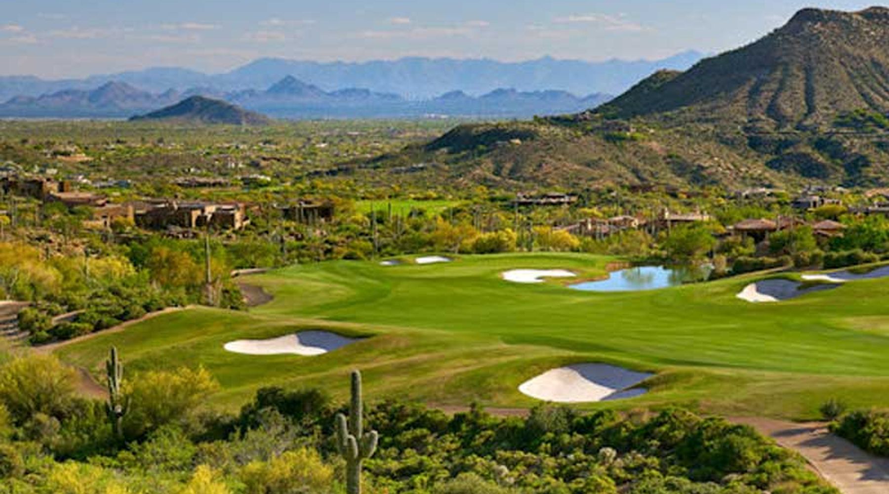 Manicured golf fairway with sand bunkers and a pond ringed by saguaro-studded desert hills