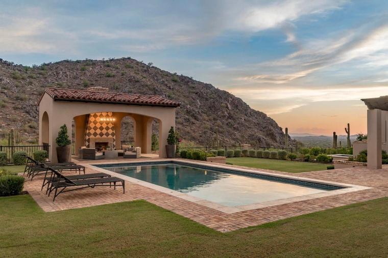 Rectangular pool and tile-roofed cabana with fireplace against a saguaro hillside at sunset