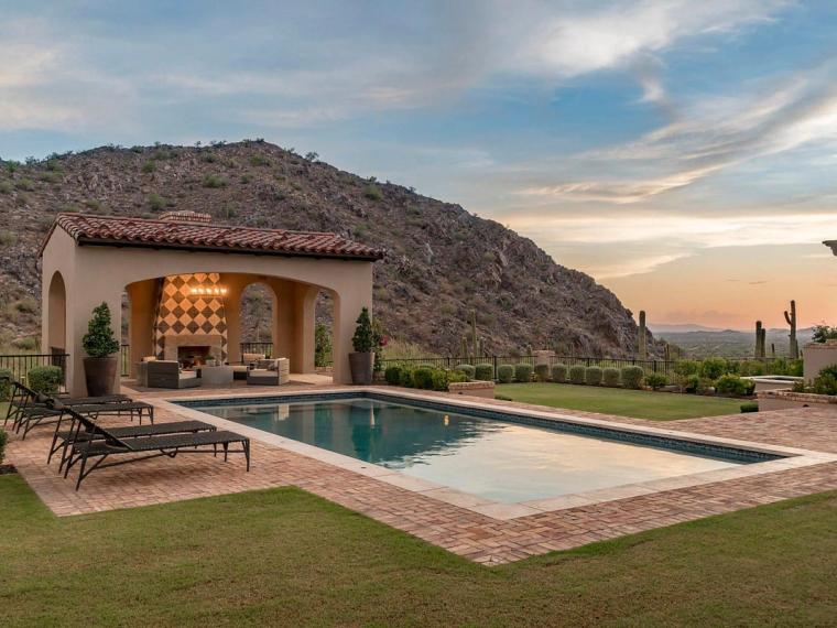 Rectangular pool and tile-roofed cabana with fireplace against a saguaro hillside at sunset