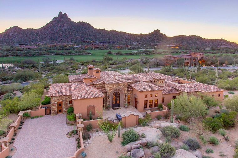 Aerial tile-roofed stone estate at dusk with a rocky peak and golf course behind
