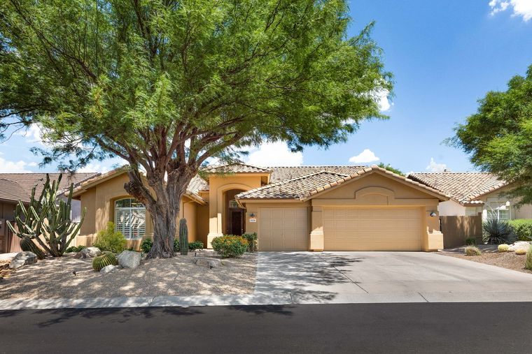 Single-story tan stucco house with tile roof and mesquite shading a gravel yard