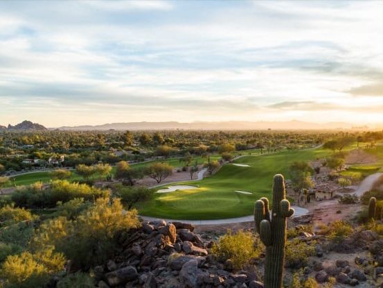 Golf holes threading between desert brush and saguaro at sunrise, low hills and a bright horizon beyond