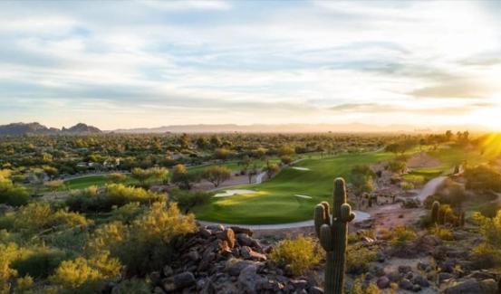 Golf holes threading between desert brush and saguaro at sunrise, low hills and a bright horizon beyond