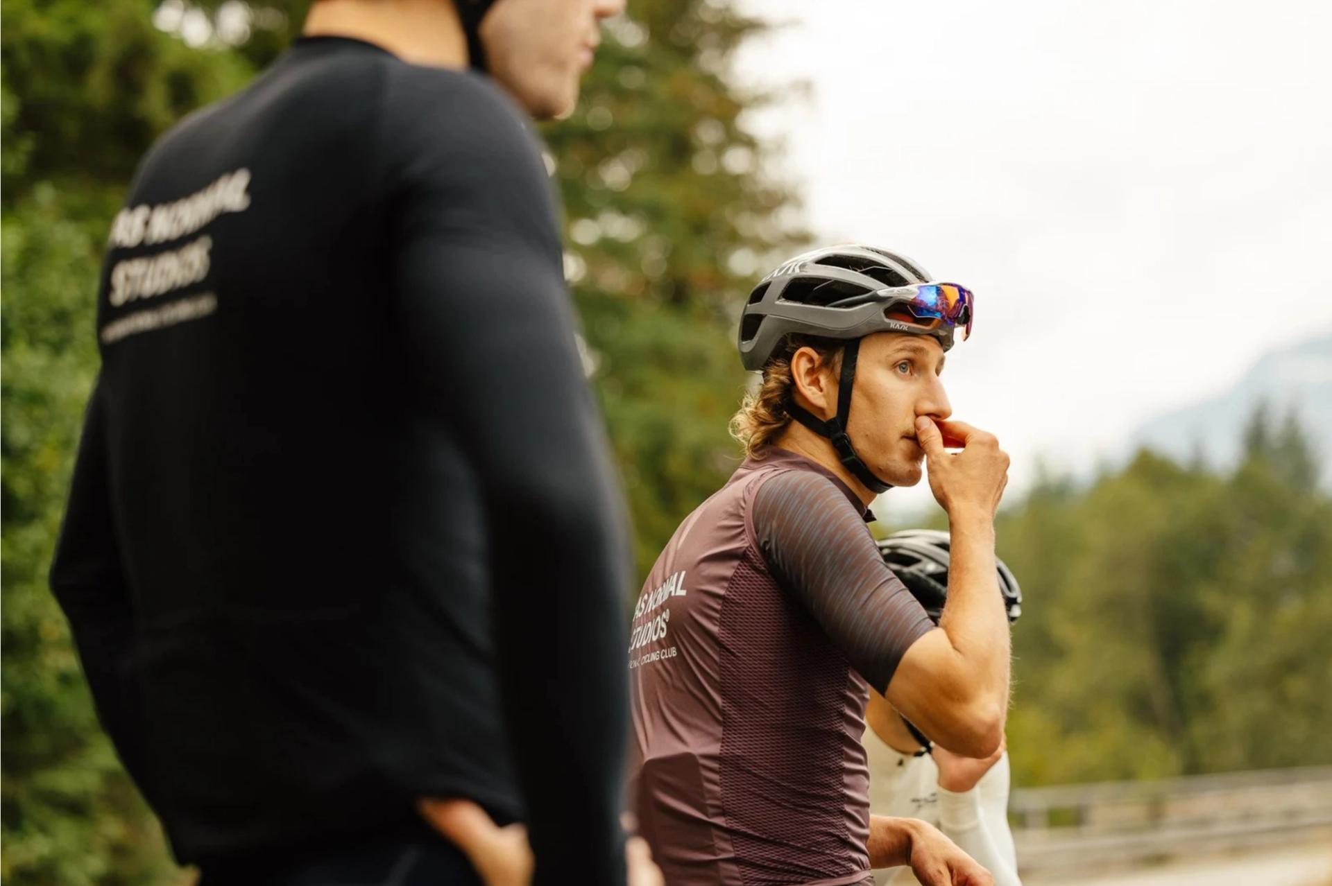 A cyclist wearing Par Normal Studios short sleeve jersey and Pas Normal Studios gilet looking out into the distance. 