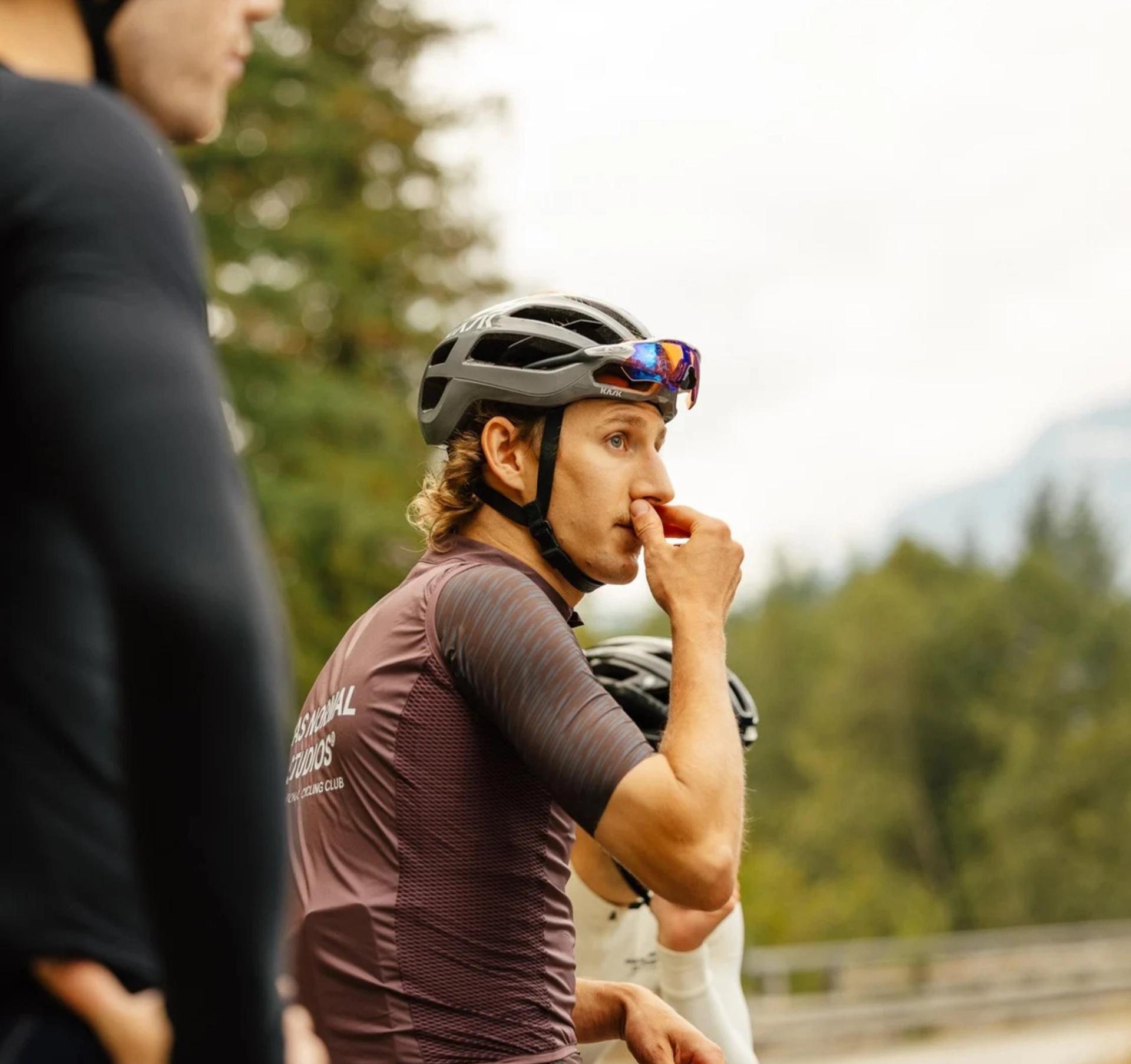 A cyclist wearing Par Normal Studios short sleeve jersey and Pas Normal Studios gilet looking out into the distance. 