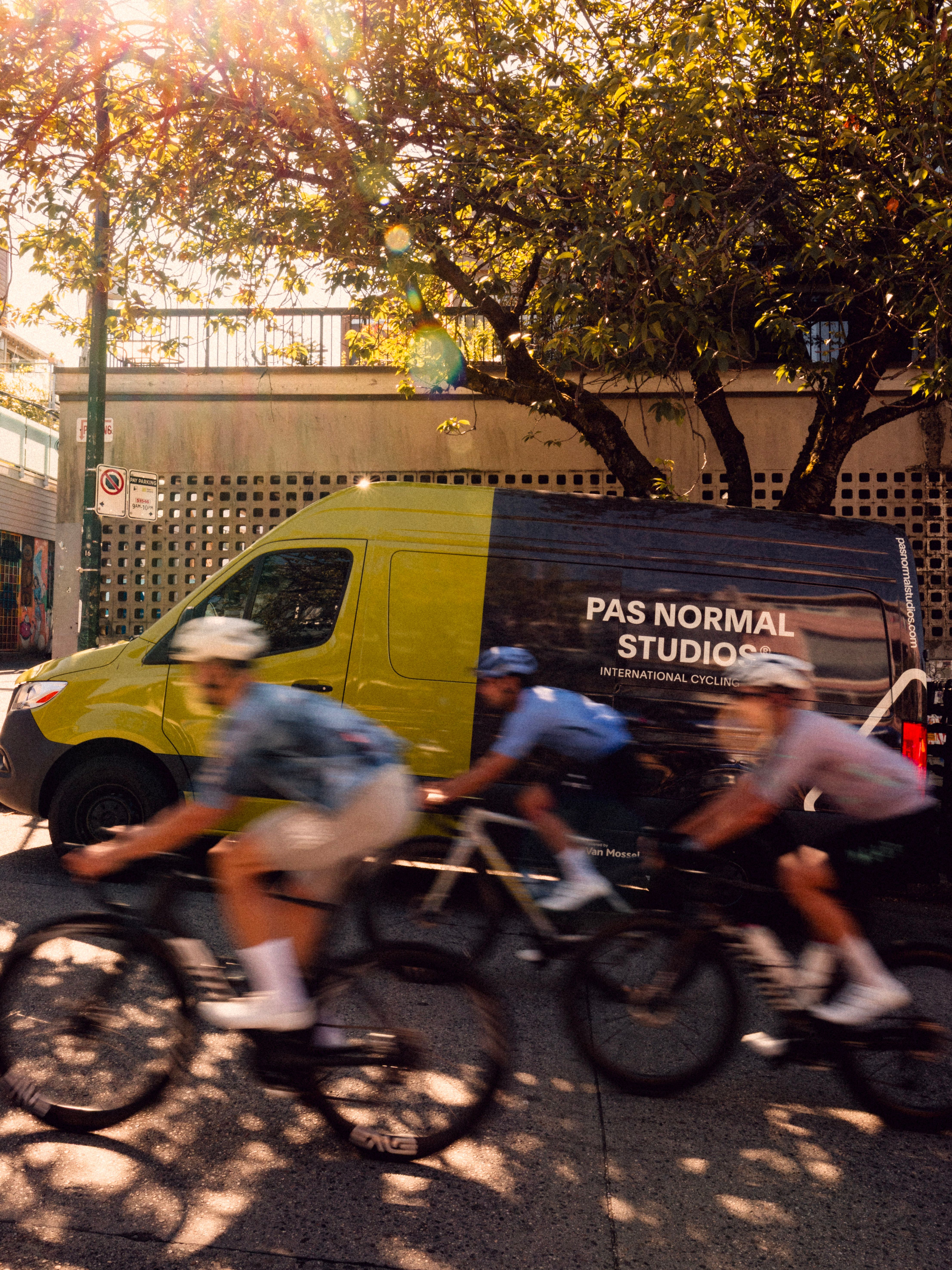 cyclists riding in front of the Pas Normal Studios Van