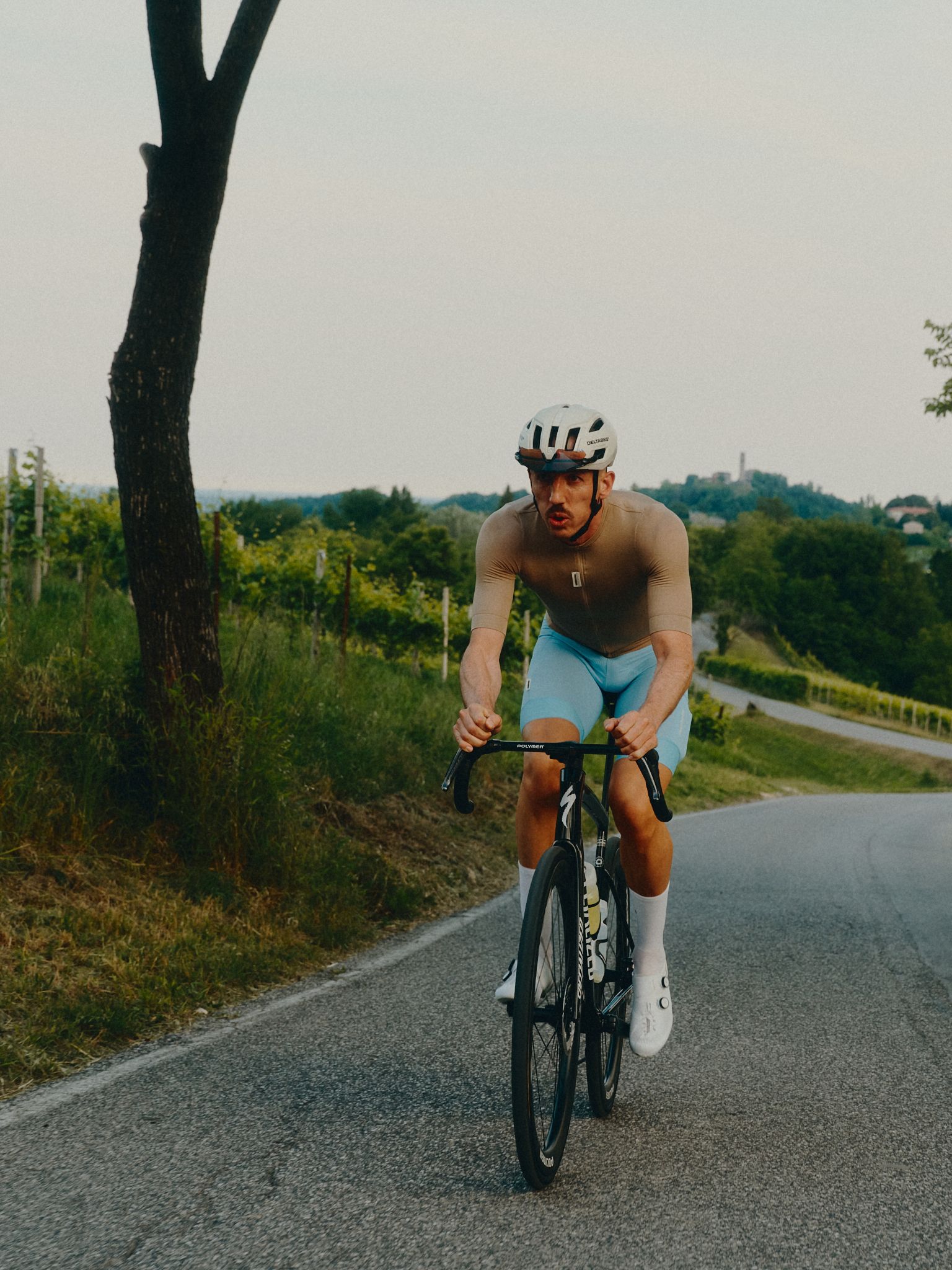 Cyclist in Pas Normal Studios kit climbing a coastal road