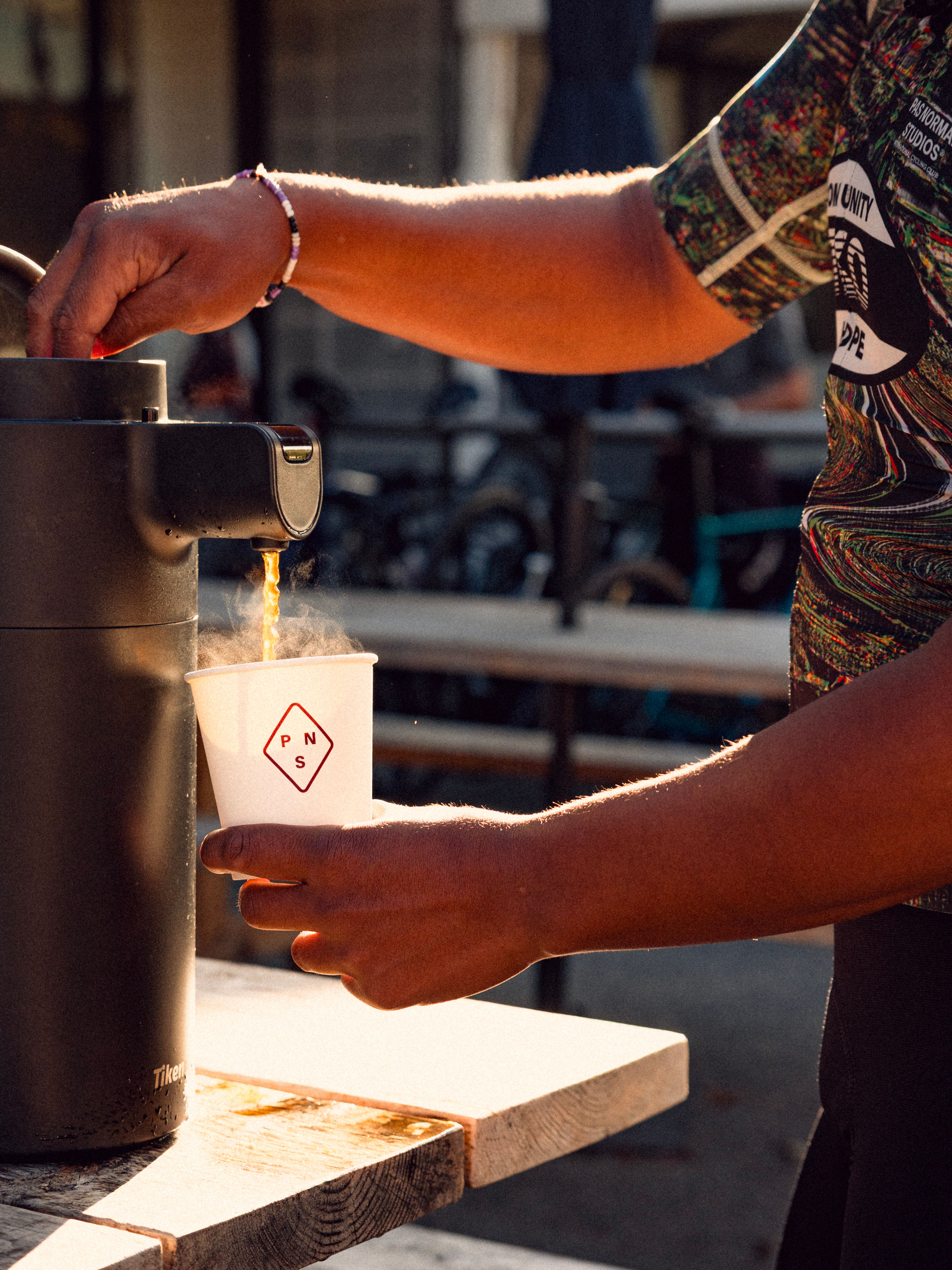 Cyclist pouring coffee with a Pas Normal Studios Branded cup