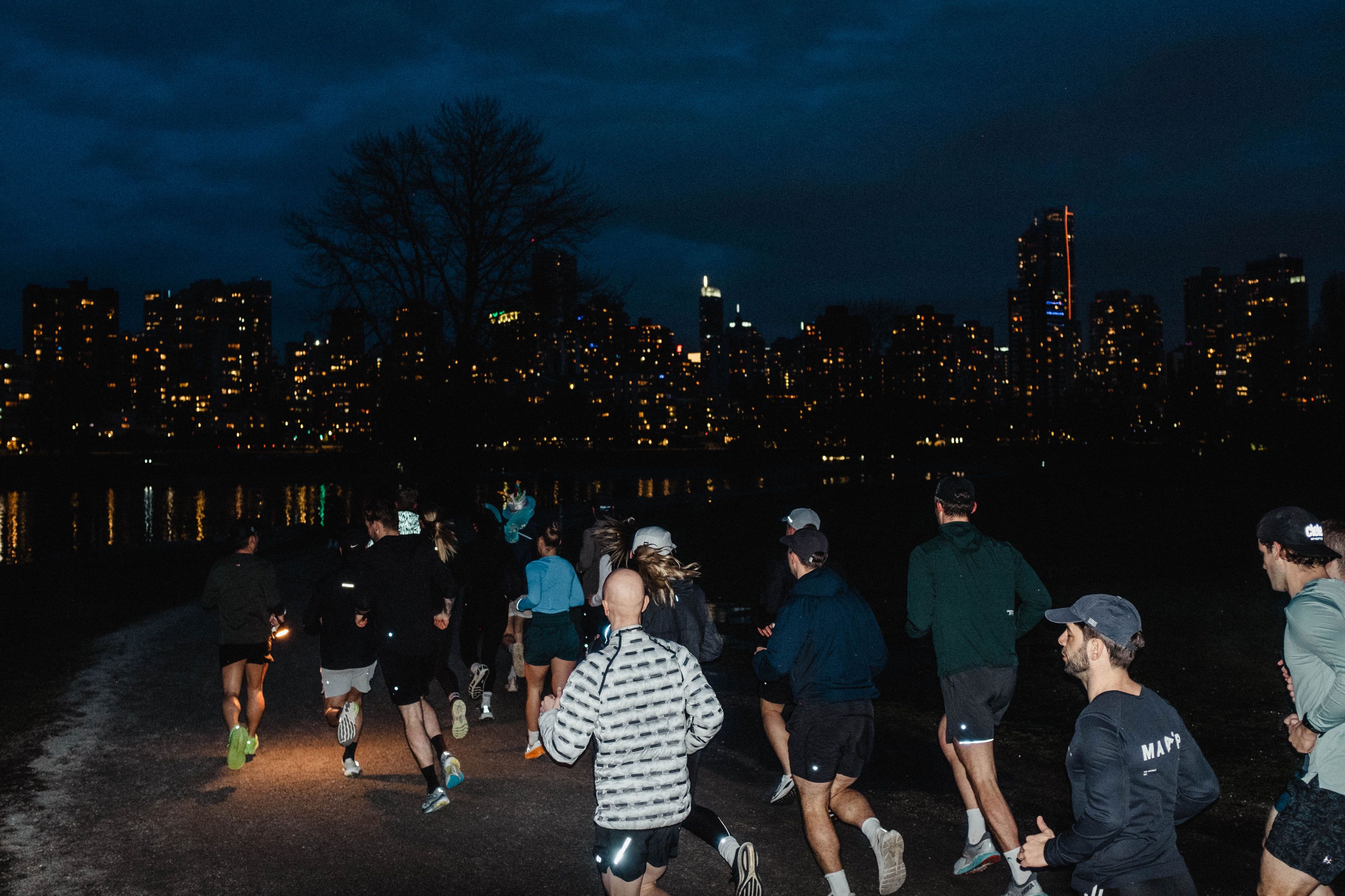 Enroute run club group night run along the water with the Vancouver skyline lit up behind