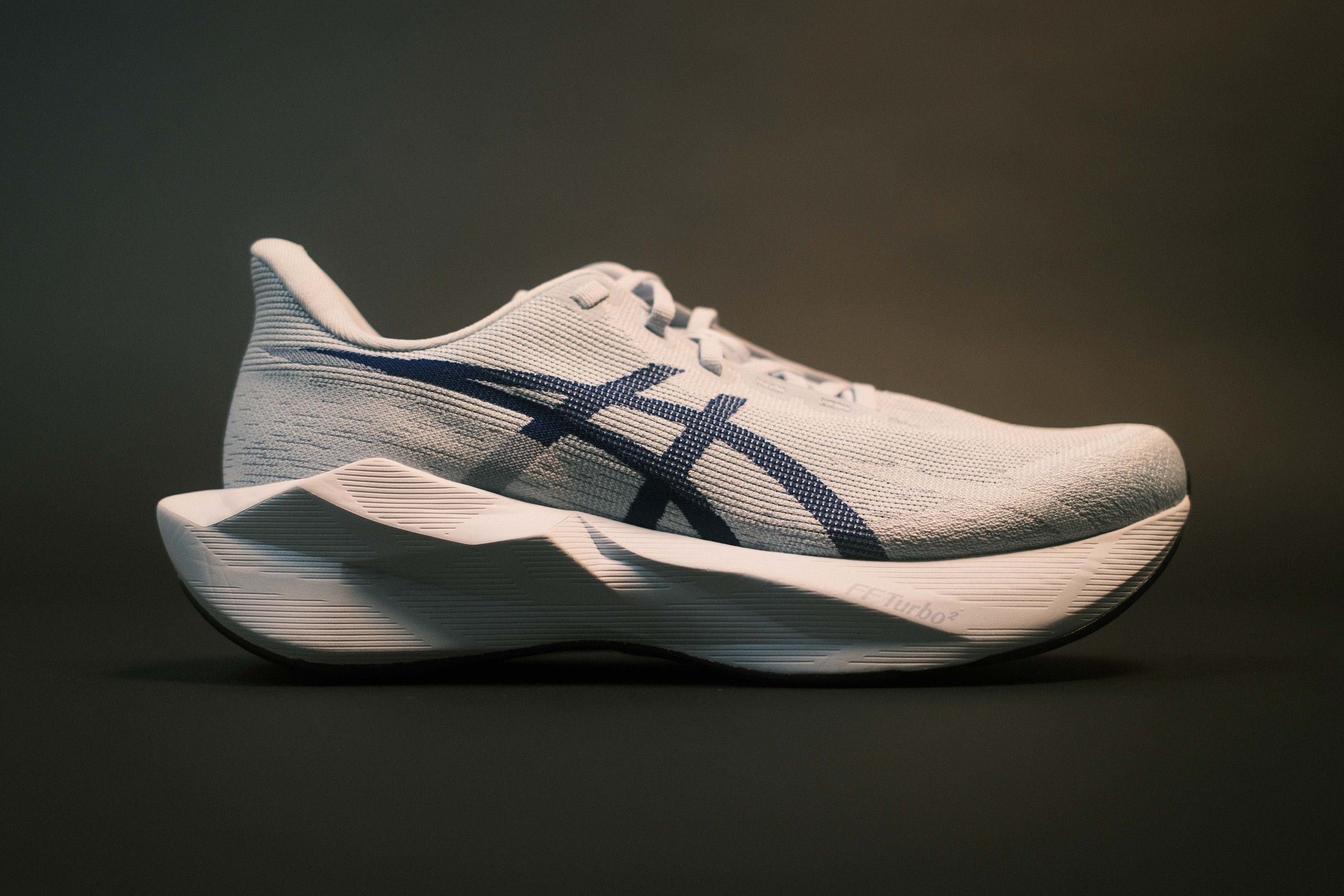 ASICS Novablast 6 in white with a navy stripe, side view on a dark studio background