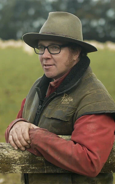 a man leaning against a wooden fence wearing a hat and glasses