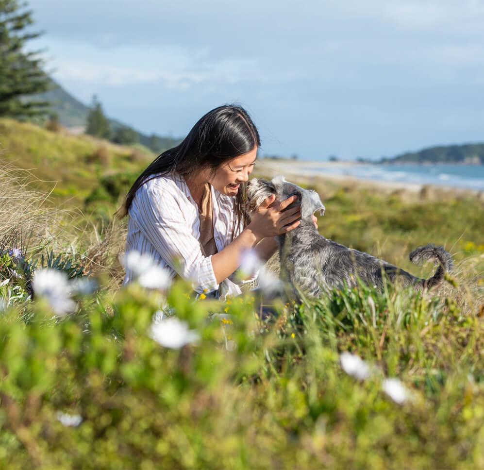 Young woman smiling giving her miniature schnauzer nose kisses infront of Mount Maunganui Young woman smiling giving her miniature schnauzer nose kisses infront of Mount Maunganui