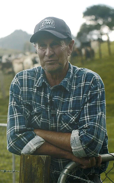 a man wearing a kiwi hat leans on a fence