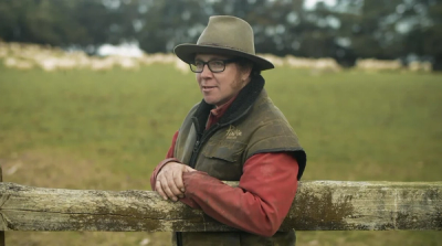 a man leaning against a wooden fence wearing a hat and glasses