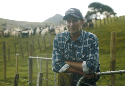 a man wearing a kiwi hat leans on a fence