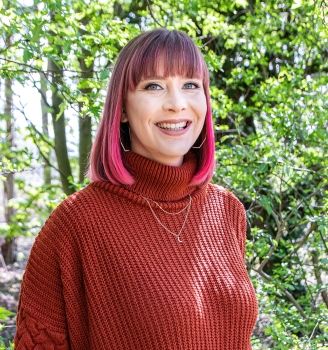 Holly, a bright haired woman, standing in front of trees