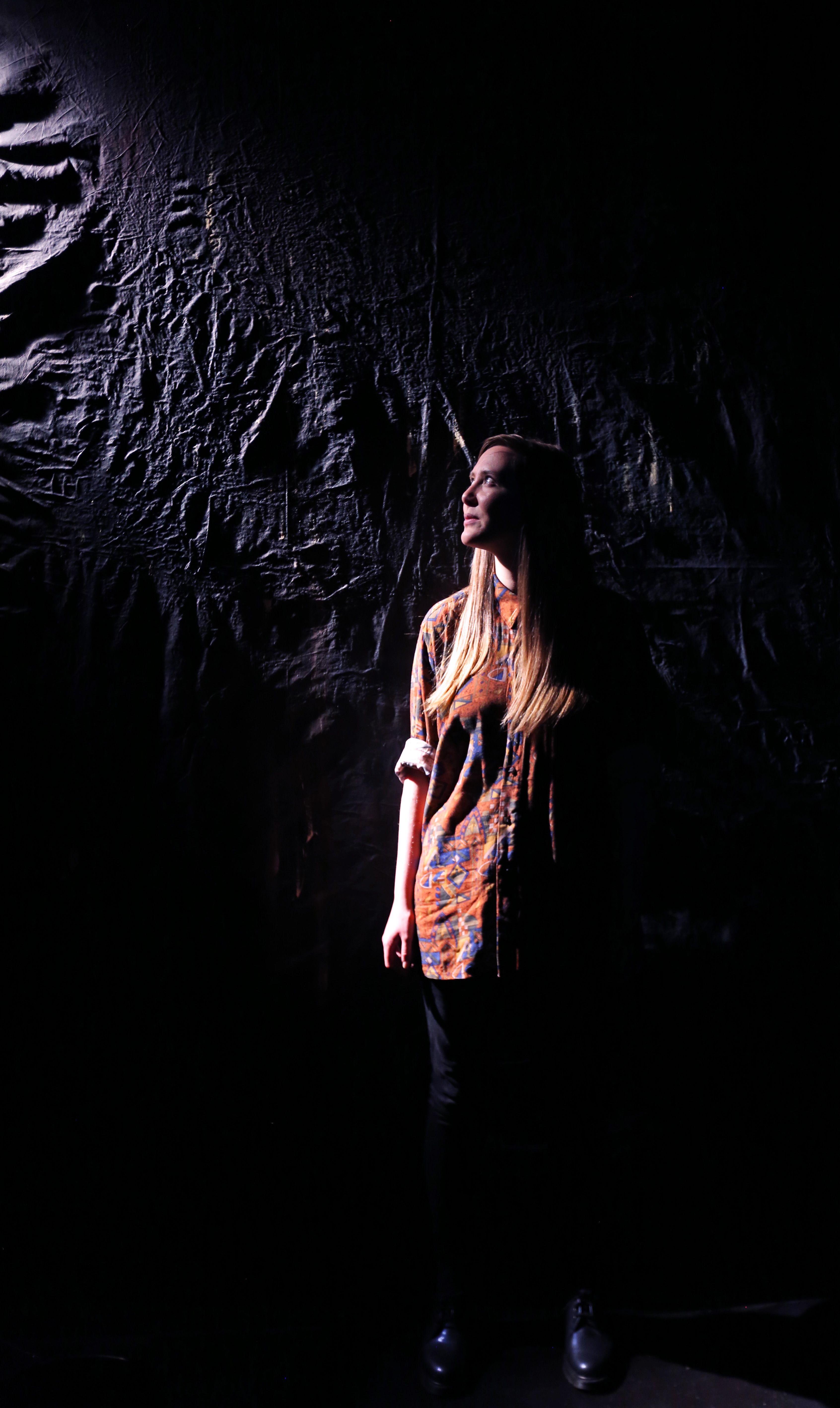 Holly standing in front of a dark backdrop - a promo image for her show Tensile Strength (or How to Survive at Your Wit's End)
