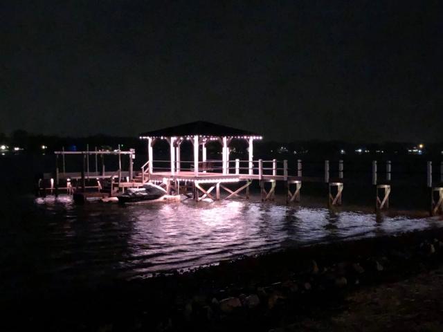 A covered boathouse lit in warm white at night