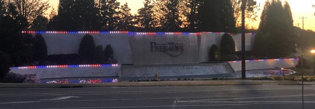A neighborhood entrance wall lit in red, white and blue at dusk