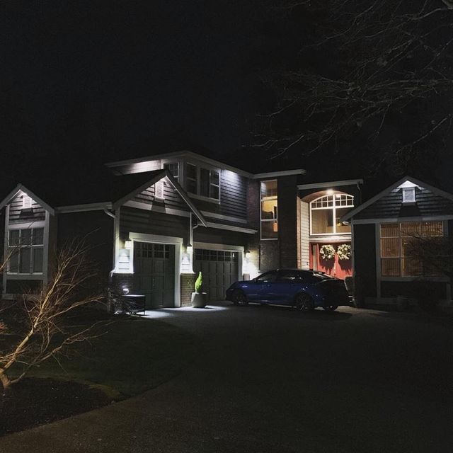 A craftsman home with the driveway lit by soffit down lights