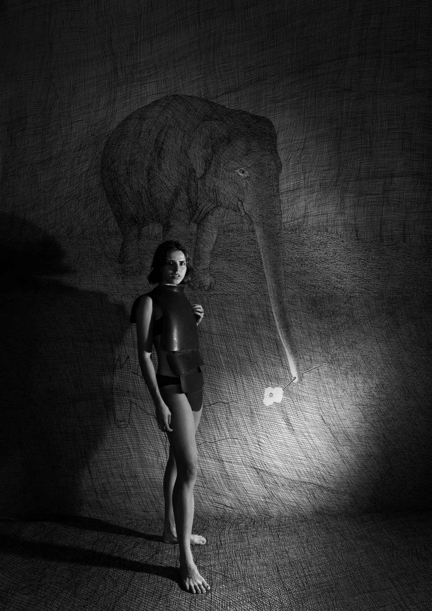 A woman in armor-like attire stands beside a textured wall with a large etched elephant.