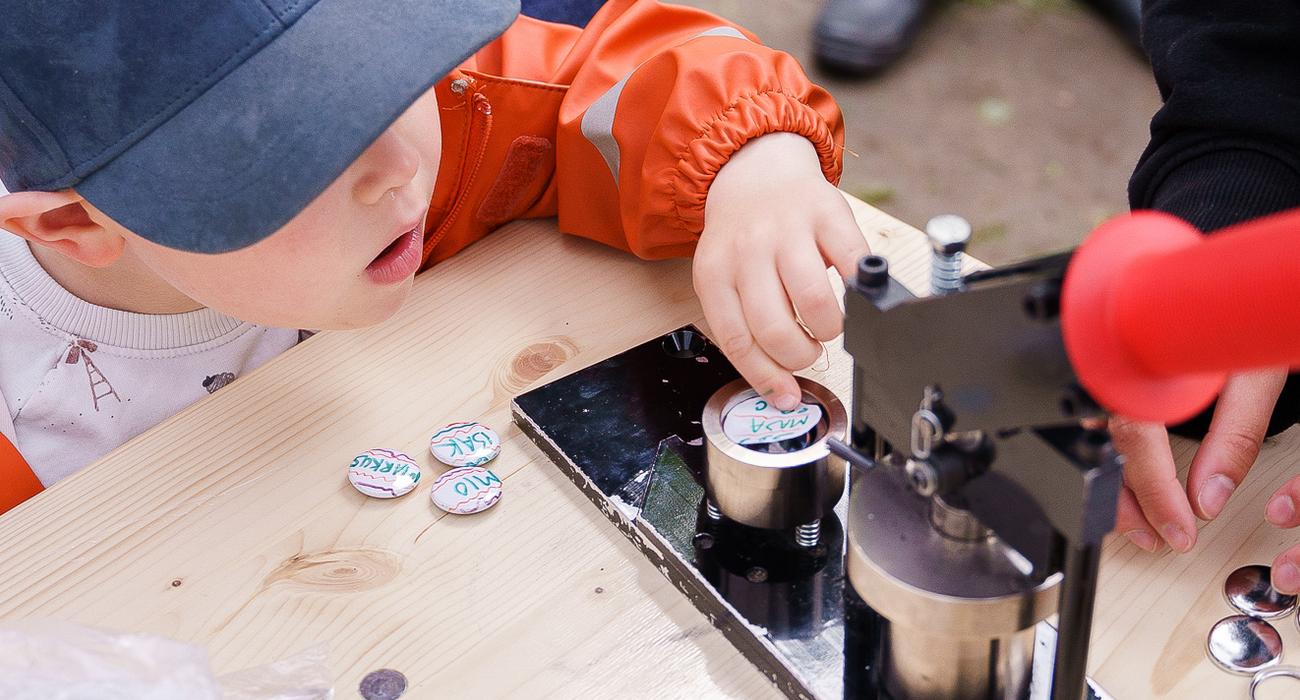 Bilda av et barn som legger en button i buttonsmaskinen.