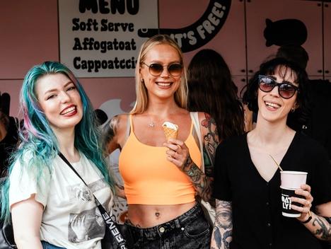 Bilde av tre unge kvinner som smiler og koser seg på festival med is og kaffe.