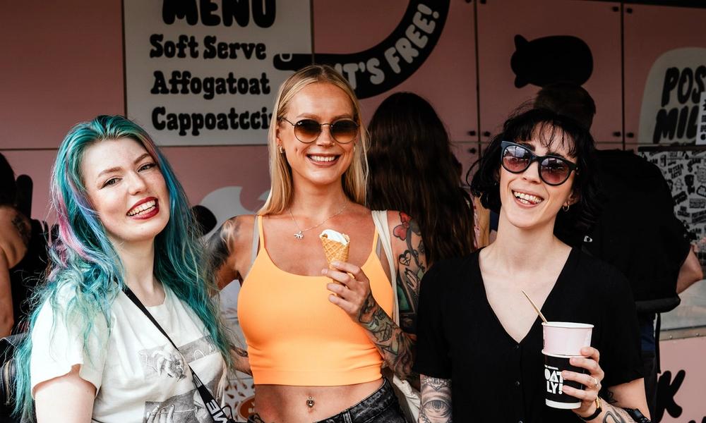 Bilde av tre unge kvinner som smiler og koser seg på festival med is og kaffe.